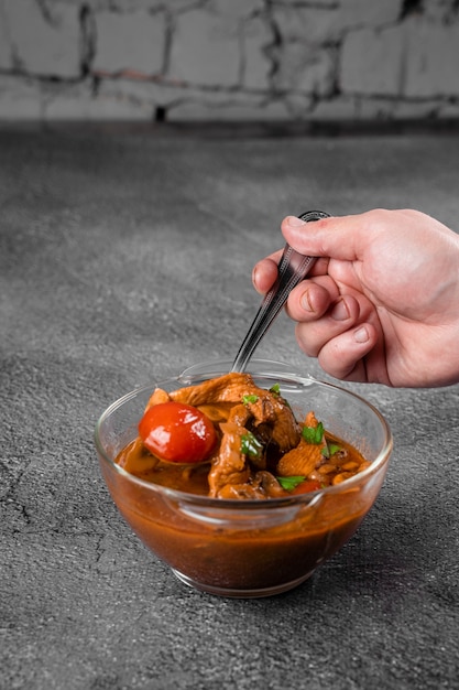 Sopa con carne, champiñones, tomates en recipiente transparente sobre superficie gris. Apetitoso y espeso y satisfactorio tom yam.