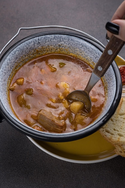 Sopa con carne y verduras en una olla sobre un fondo oscuro