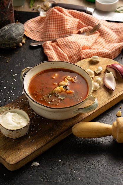 Sopa caseira com bolinhos, creme de leite, cebola e especiarias. Uma tigela de sopa, uma colher, uma toalha, um rolo de massa e ingredientes em uma mesa preta.