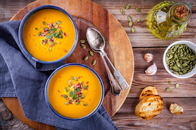 Sopa casera de calabaza de otoño con semillas de calabaza, tocino y albahaca sobre fondo de madera