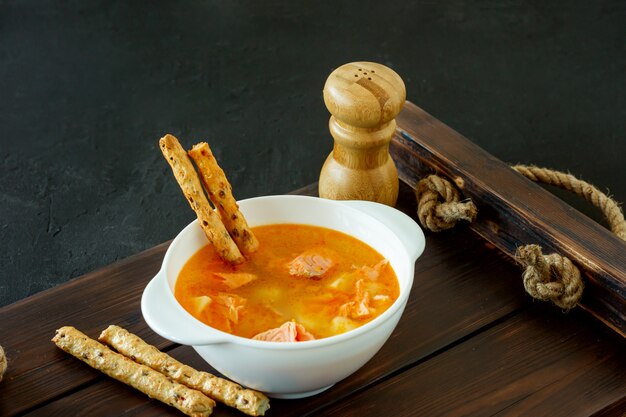 Sopa casera de salmón con palitos de pan en bandeja de madera.