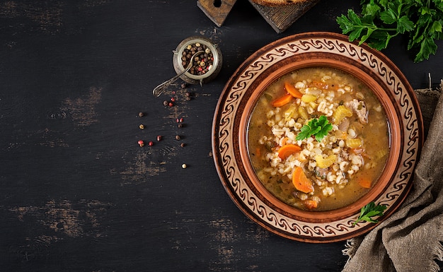 Sopa de cebada con zanahorias, tomate, apio y carne sobre un fondo oscuro. Vista superior.