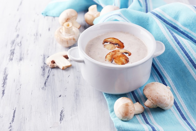 Sopa de champiñones en una olla blanca, en una servilleta de mesa de madera