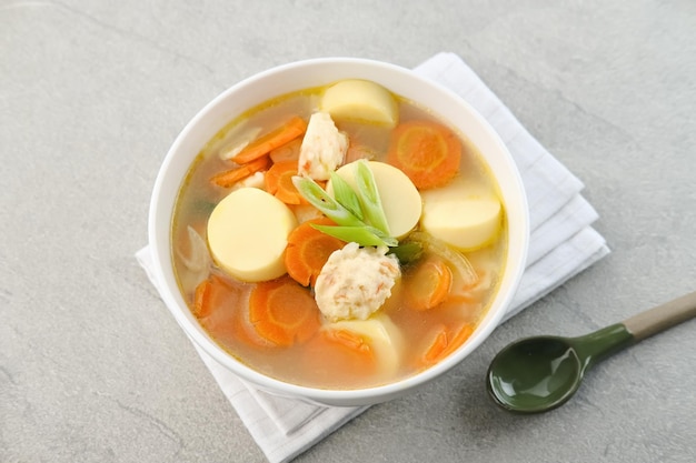 Sopa clara con huevo, tofu, zanahoria y albóndigas de camarones Servido en un tazón blanco sobre fondo gris