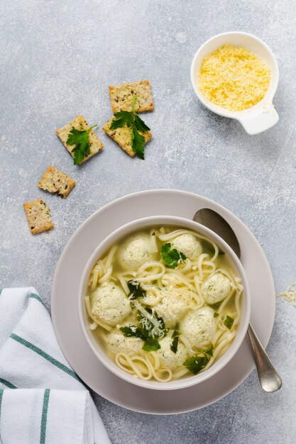 Sopa com almôndegas de frango e macarrão de ovo com queijo parmesão e salsa. Comida italiana infantil com massas e carnes. Cozinha tradicional italiana. Vista do topo.