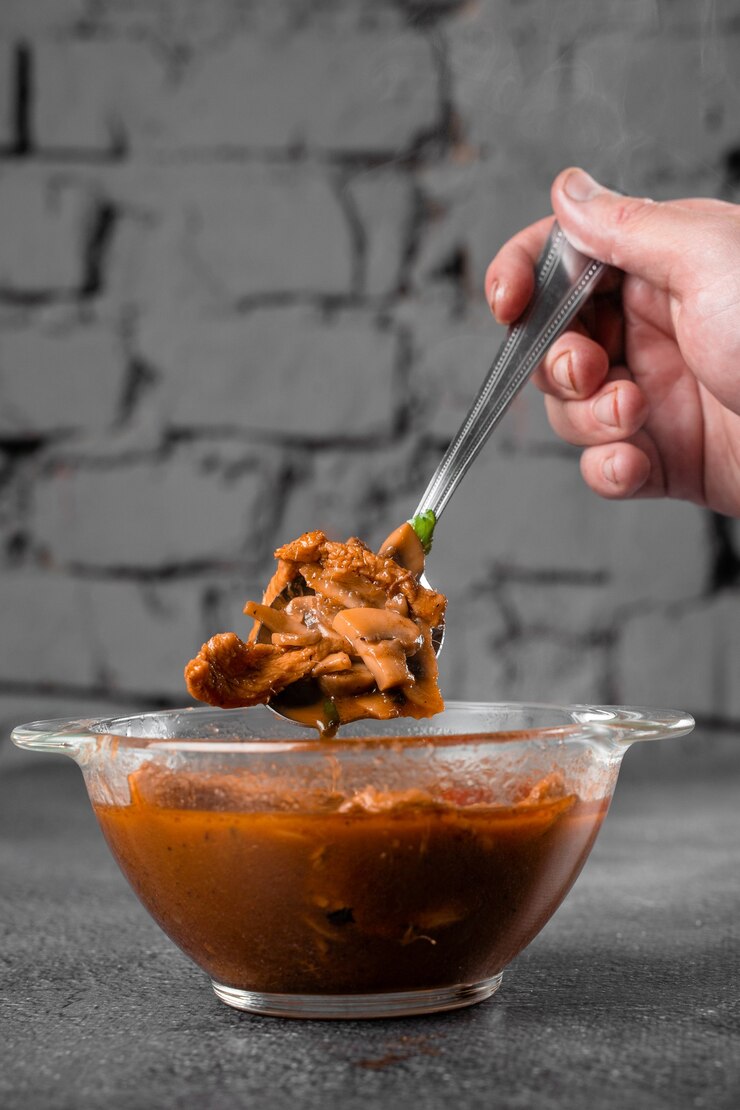 Sopa com carne, cogumelos, tomate em uma tigela transparente na superfície cinza. Espesso apetitoso satisfazendo tom yam.
