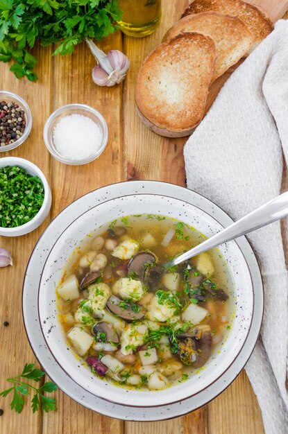 Sopa com feijão, cogumelos e bolinhos de massa em uma tigela sobre uma superfície de madeira escura com ervas e alho