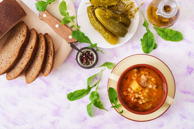 Sopa com pepinos em conserva e cevada perolada - rassolnik em um fundo claro.