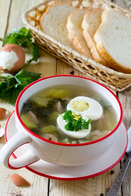 Sopa com urtiga fresca, ovo, carne e batata. Folha de urtiga fresca na mesa da cozinha um fundo rústico.