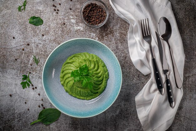 Sopa de crema de aguacate y espinacas verdes en una placa azul con perejil y eneldo contra una mesa de piedra gris