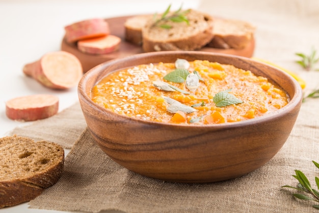 Sopa de crema de batata o batata con semillas de sésamo en un recipiente de madera sobre una superficie de madera blanca con textiles de lino