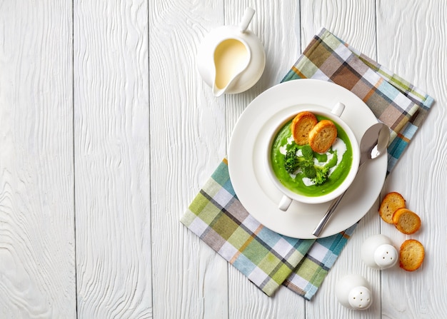 Sopa de crema de brócoli en un tazón de sopa blanco servido con rebanadas tostadas de baguette y crema fresca, vista desde arriba, flatlay, espacio de copia