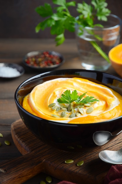 Sopa crema de calabaza con crema y semillas de calabaza en la mesa de madera.