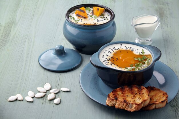 Sopa de crema de calabaza con crema, semillas de comino negro, hierbas y pan tostado sobre una mesa de madera azul claro. Vacaciones de invierno