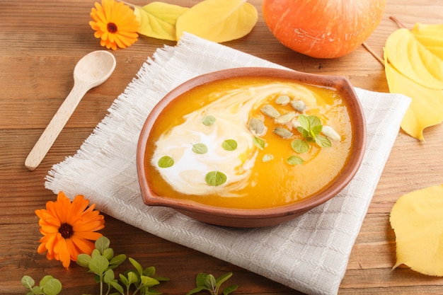 Sopa de crema de calabaza tradicional con semillas en un recipiente de arcilla sobre una superficie de madera marrón con servilleta de lino. vista lateral.