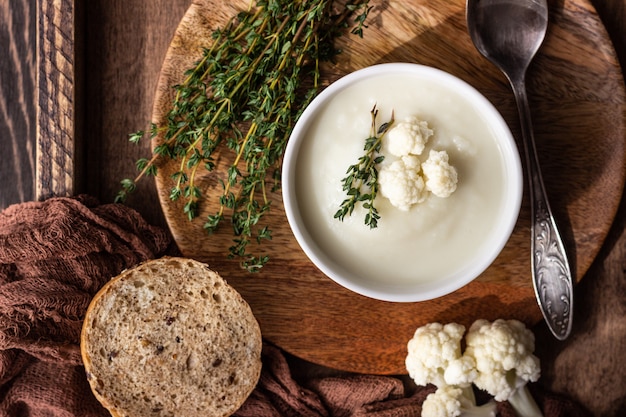 Sopa de crema de coliflor decorar con coliflor fresca, tomillo y pan en un tazón de cerámica blanca.