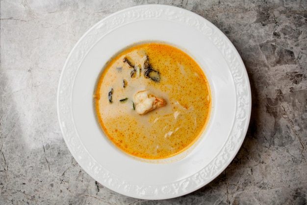 Sopa de crema cremosa con gambas y hierbas, en un plato naranja, sobre un fondo de mármol.