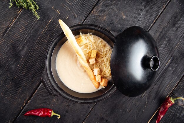 Sopa de crema con galletas y queso rallado en un recipiente de hierro fundido sobre la madera negra