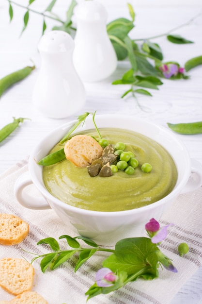 Sopa crema de guisantes verdes con picatostes en un tazón blanco