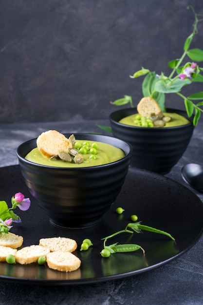 Sopa crema de guisantes verdes con picatostes en un tazón negro