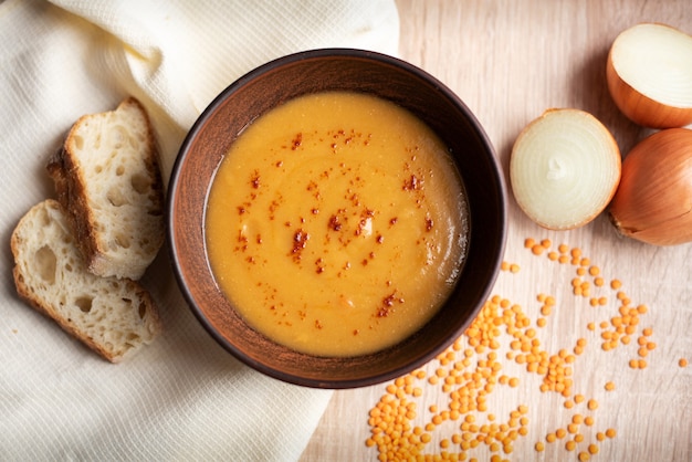 Sopa de crema de lentejas rojas vegetariana caliente con zanahoria, cebolla y pan en la mesa de madera, de cerca, vista superior.