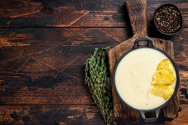 Sopa de crema de papa con papas fritas en sartén sobre tabla de madera.