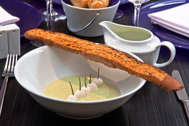 sopa de crema de pistacho con bolas de queso brie acompañadas de pan baguette en una mesa de restaurante