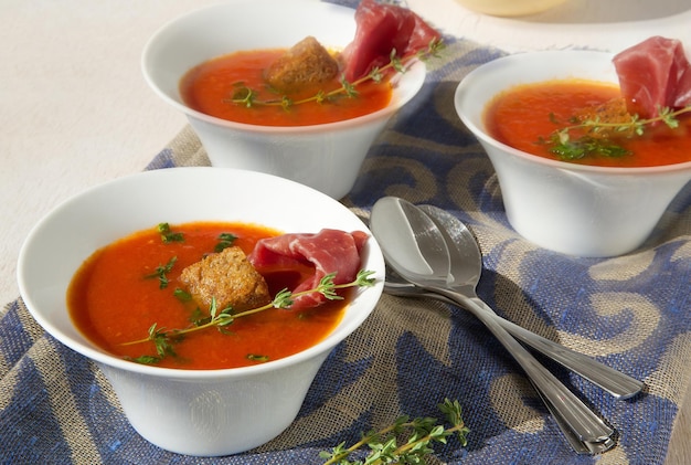 Sopa de crema de tomate con bresaola y tomillo en un plato blanco sobre un saco azul oscuro