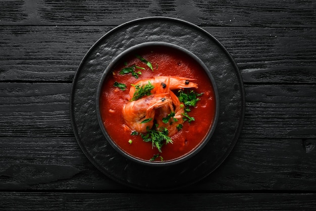 Sopa de crema de tomate con camarones en un tazón negro. Menú de mariscos. Vista superior. Estilo rústico.