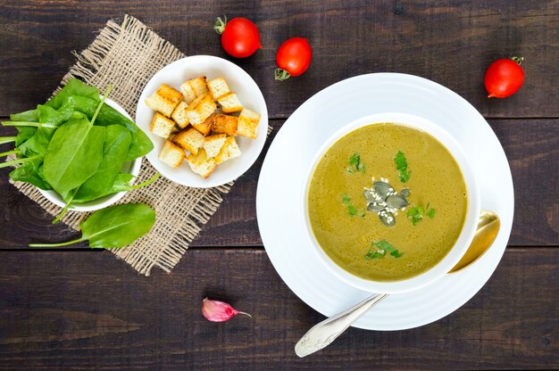 Sopa de crema de verduras con espinacas y patatas en un recipiente blanco con picatostes de ajo en la mesa de madera oscura.