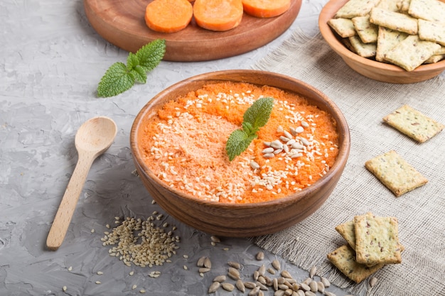 Sopa de crema de zanahoria con semillas de sésamo y aperitivos en un recipiente de madera sobre un hormigón gris. Vista lateral, de cerca.