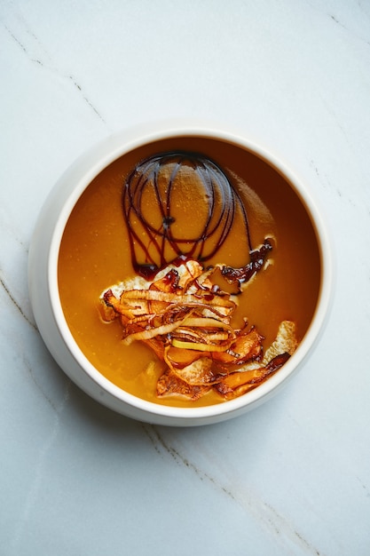 Foto sopa creme cor laranja com cogumelos selvagens secos em uma tigela de cerâmica sobre uma superfície de mármore. almoço vegetariano. vista superior, espaço de cópia