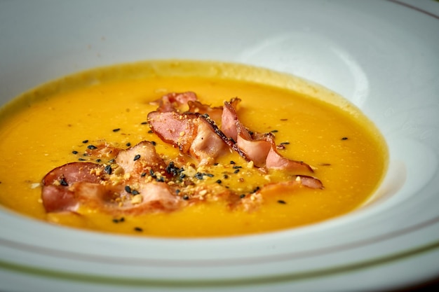 Sopa creme de abóbora com bacon em um prato fundo de madeira