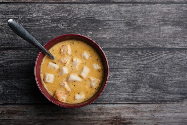 Sopa creme de abóbora com bolachas na tigela com uma colher na mesa de madeira