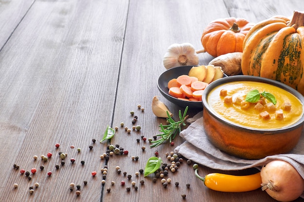 Sopa creme de abóbora com cenoura e gengibre em uma tigela de cerâmica na madeira