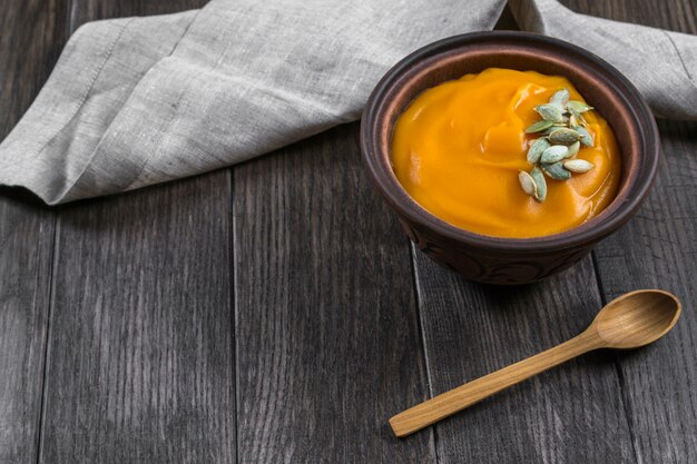 Sopa creme de abóbora com sementes em uma tigela de barro na mesa de madeira escura