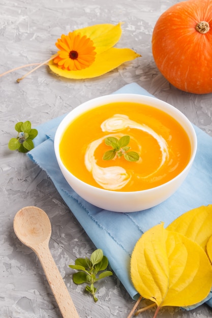 Sopa creme de abóbora tradicional em tigela branca sobre um fundo cinza de concreto com guardanapo azul.