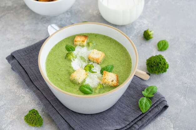 Sopa creme de brócolis com manjericão fresco e croutons em uma tigela sobre um fundo cinza de concreto