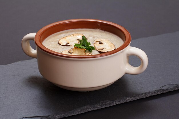 Sopa creme de cogumelos caseiros em uma tigela de porcelana com cogumelos fatiados na placa de pedra preta.