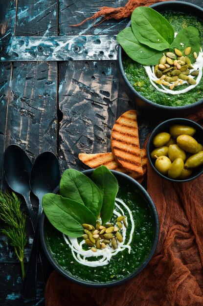 Sopa creme de espinafre verde com creme e sementes de abóbora em uma tigela preta comida saudável vista superior estilo rústico