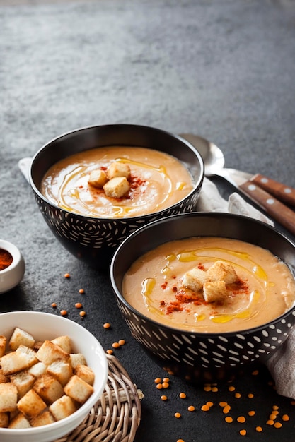 Sopa creme de lentilha com páprica e crouton em tigelas de cerâmica pretas sobre fundo escuro. Copiar espaço