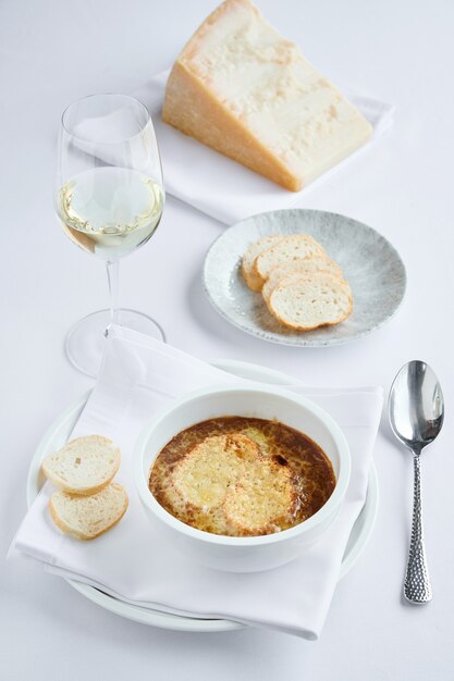 Sopa cremosa de cebolla francesa con picatostes y queso parmesano con copa de vino blanco seco sobre la mesa