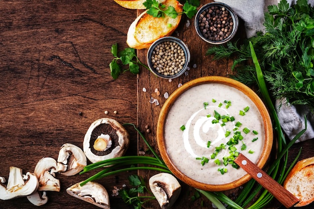 Sopa cremosa de champiñones con migas de pan y cebollino sobre fondo de madera rústica