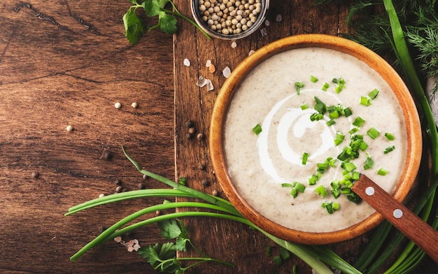 Sopa cremosa de champiñones con picatostes, especias y cebollino sobre fondo de mesa de madera rústica