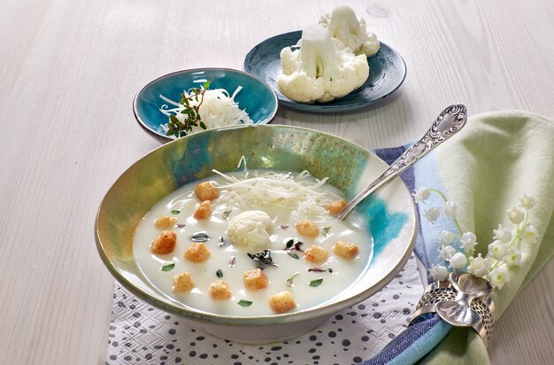 Sopa cremosa de coliflor en una taza azul con picatostes y parmesano