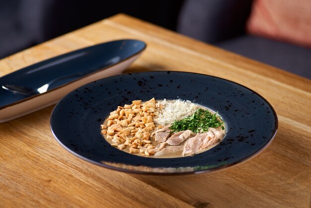 Sopa cremosa com carne, nozes e vegetais. Jantar delicioso em close-up de prato em mesa de madeira