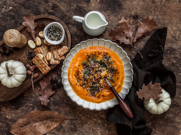 Sopa cremosa de abóbora com sementes de gergelim e abóbora e biscoito em uma mesa de madeira vista superior