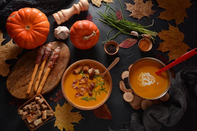 Sopa cremosa de abóbora e batata doce (batata) com bacon em fundo escuro. Uma tigela de sopa com croutons caseiros e ervas com decorações de outono.
