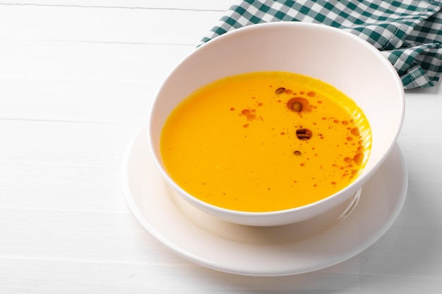 Sopa cremosa de abóbora servida em tigela sobre fundo branco de madeira