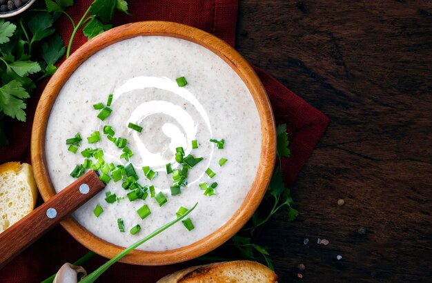 Sopa cremosa de cogumelos com croutons e cebolinha em fundo de madeira rústica